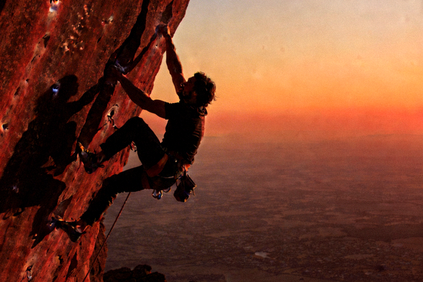攀岩者在夕阳下攀登红色岩壁的剪影，展现力量与技巧